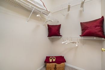 A room with a white wall and a shelf with two red pillows and a basket.